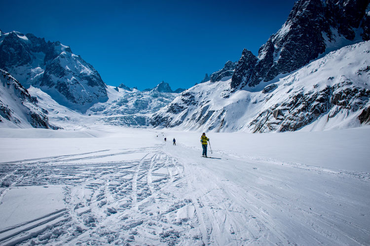 Person walking on snowy field against snowcapped mountains
