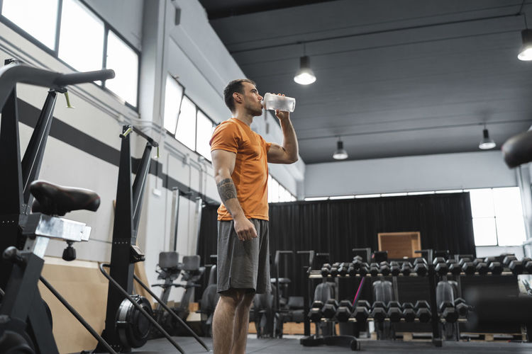 Mid adult man drinking water while standing in gym