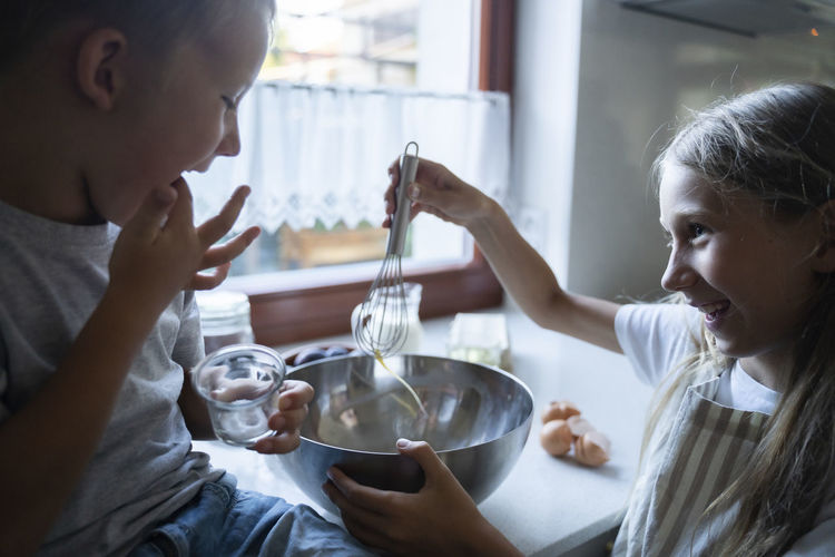 Siblings mixing ingredients for making cake in kitchen at home