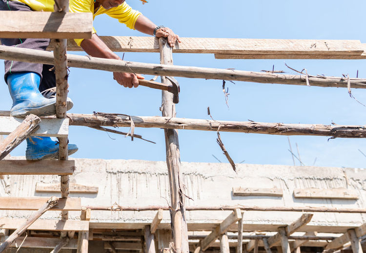 Worker hit nail on wooden stick for support second floor in building site.
