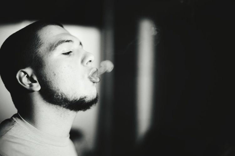 Side view of young man exhaling smoke from mouth