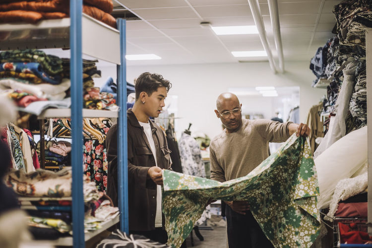 Male fashion designer with colleague examining fabric at workshop