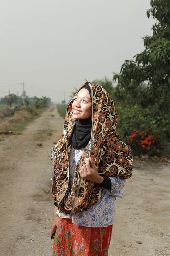 Girl wearing hijab standing on dirt road against sky
