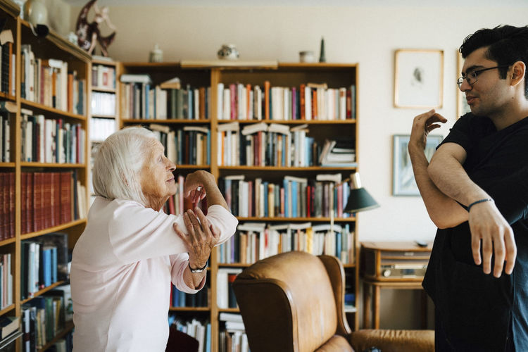 Male healthcare worker assisting senior woman to do exercise at home