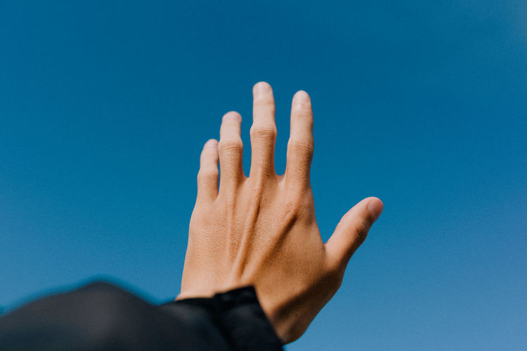 Cropped hand of man reaching towards clear blue sky