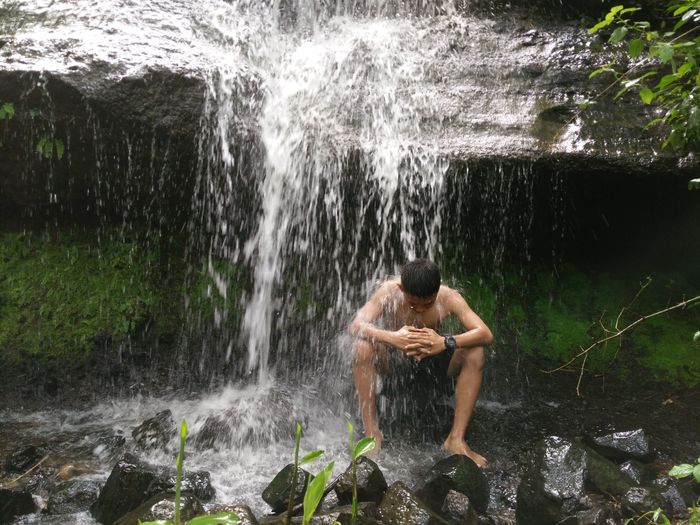 Full length of shirtless man on rock in forest