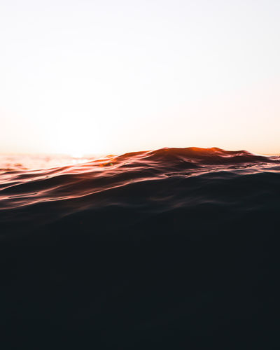 Scenic view of waves against clear sky during sunset
