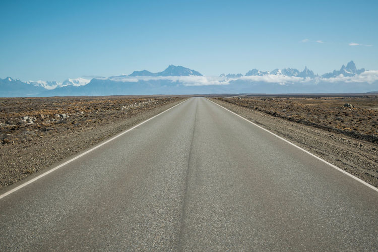 Road leading towards desert and snowcapped mountains against sky