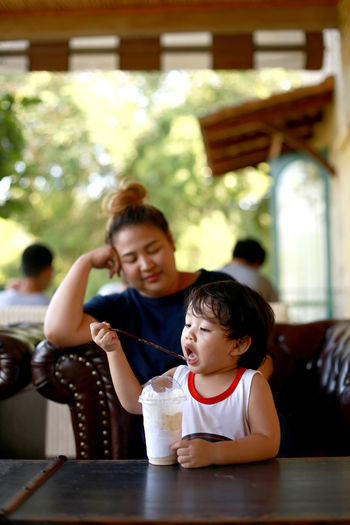Boy drinking juice with mother on table