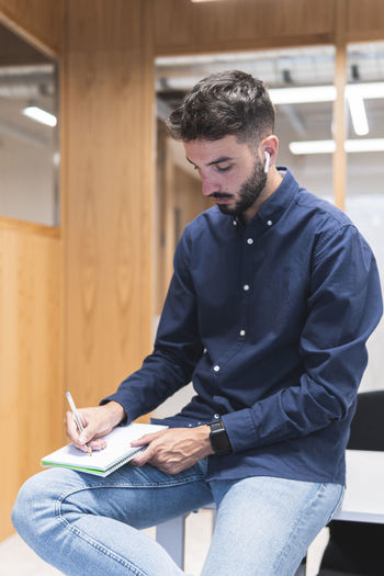 Young businessman writing in diary sitting on desk in office
