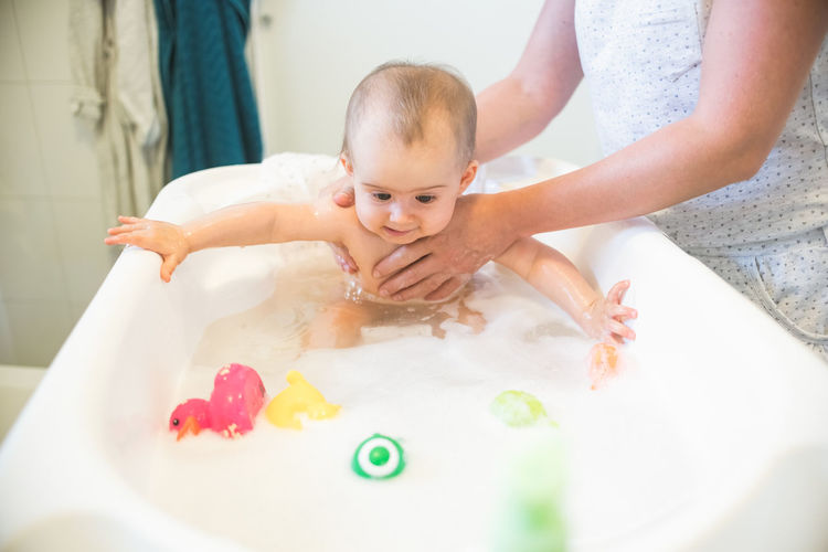 Adorable baby in plastic bathtub. mother bathing newborn, baby hygiene concept.