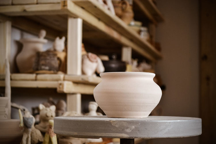 Clay pot close-up in the foreground and shelves with pottery - on the second