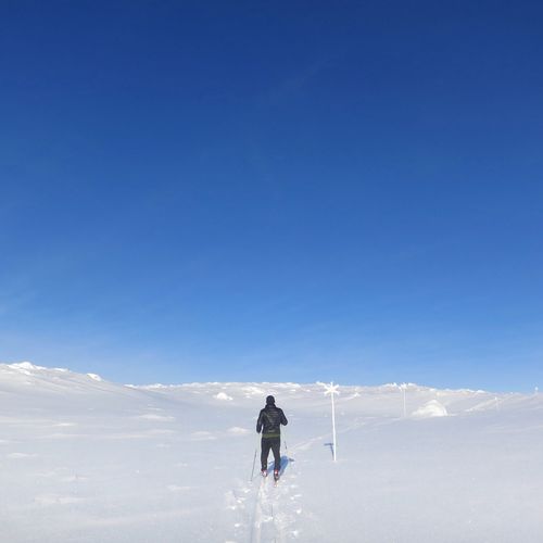Rear view of man skiing on snow covered mountain against clear sky