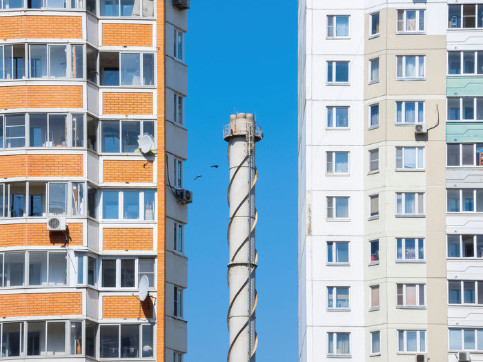 Chimney tube against a blue sky surrounded by apartment buildings