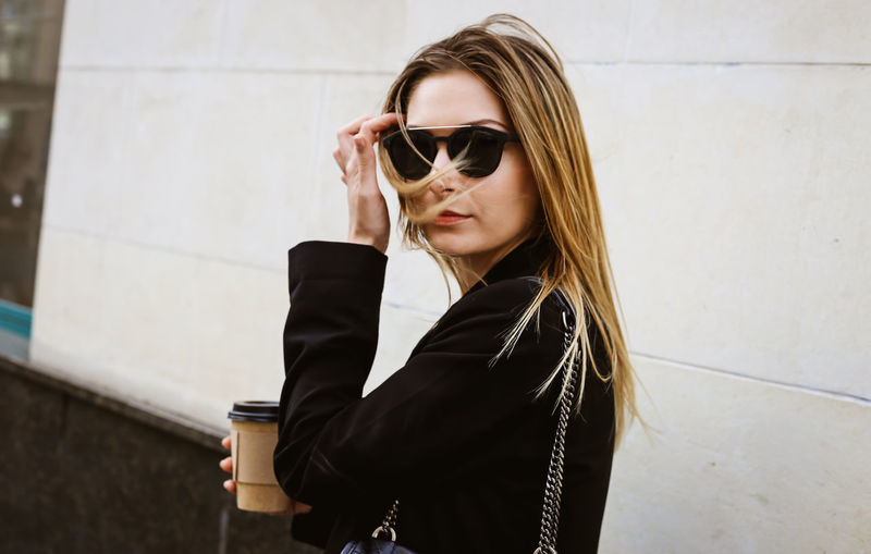Young woman wearing sunglasses against wall