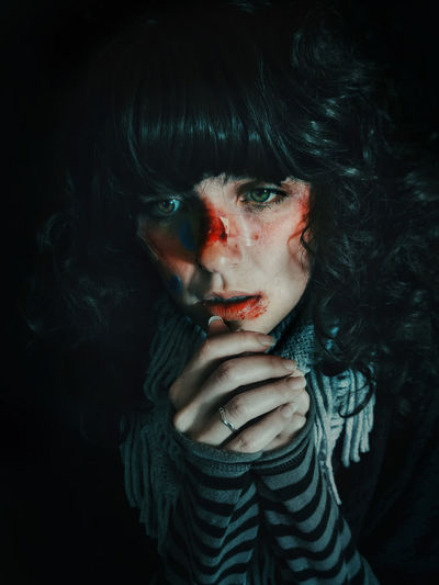 Close-up of woman with wounds on face against black background