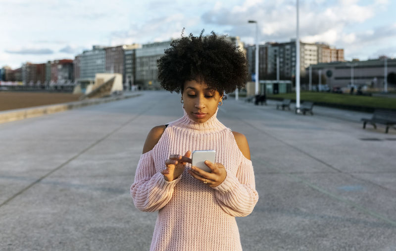 Young woman with afro hair using mobile phone while standing on street