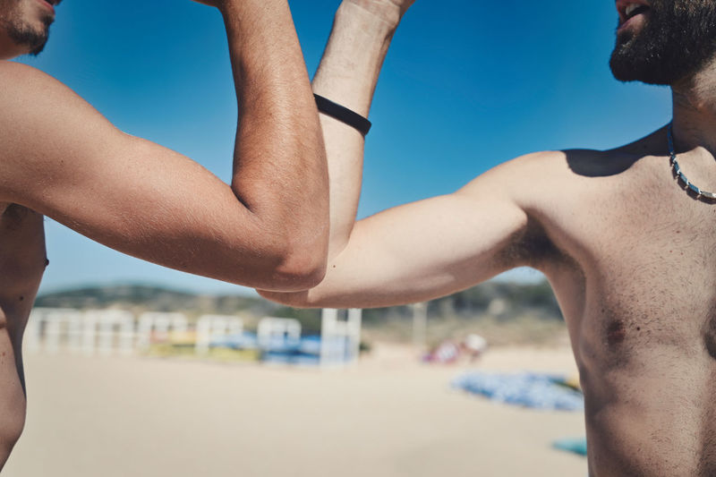 Midsection of shirtless men following social distancing with elbow bump at beach