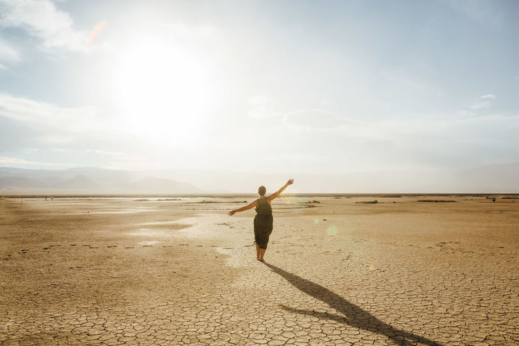 Woman with arms outstretched in desert against sky