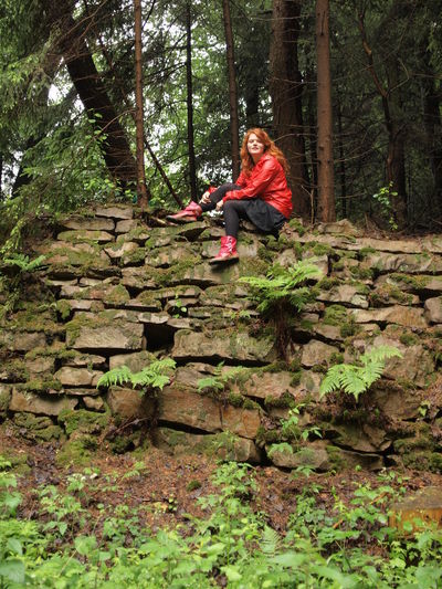 Portrait of woman sitting on stone wall in forest during monsoon