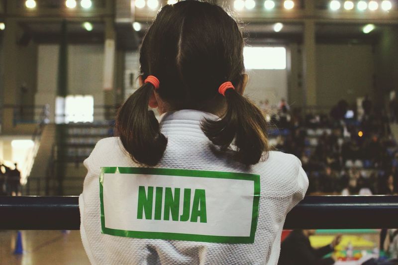 Rear view of girl with ninja text on back by railing