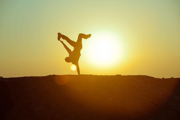 Silhouette person doing handstand against sky during sunset