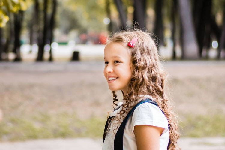 Happy schoolgirl in uniform with long hair in the park on a warm day