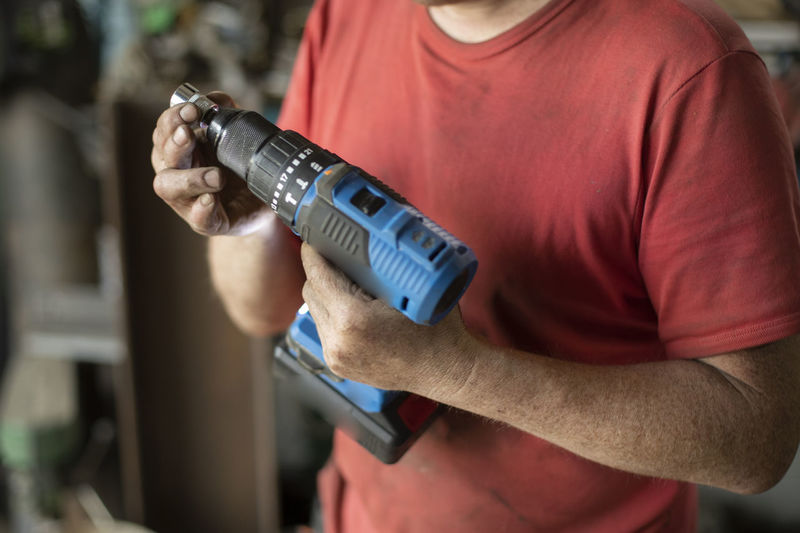 The man shows a screwdriver. a guy in a workshop with a power tool in his hand. 