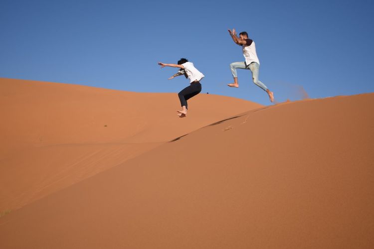 Low angle view of friends jumping in desert against clear sky