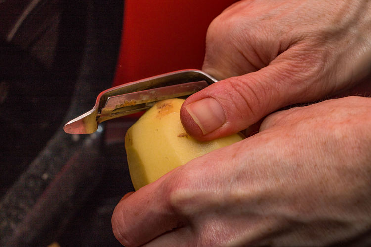 Cropped hands peeling potato