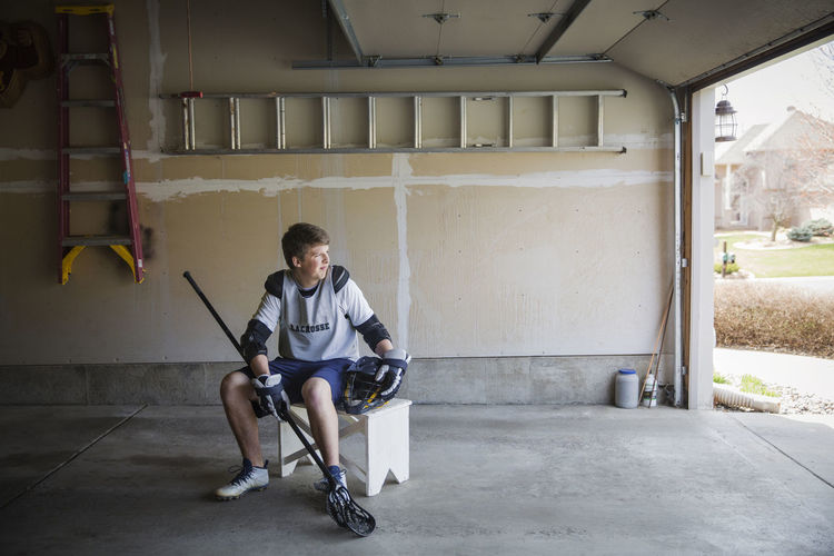 Young man holding lacrosse stick and sitting on stool