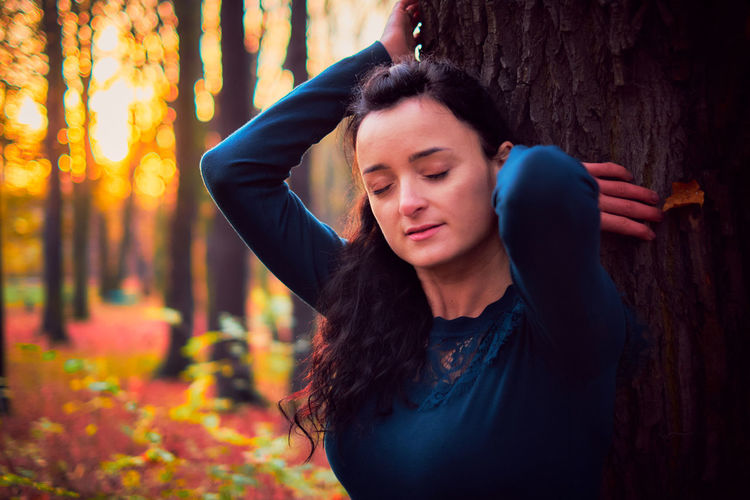 Beautiful young woman lying down on tree trunk in forest during autumn