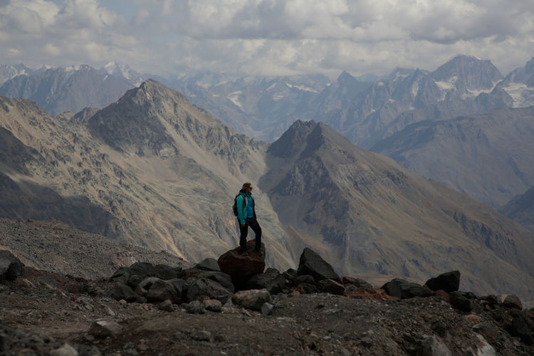 Man standing on rocks by mountains against sky