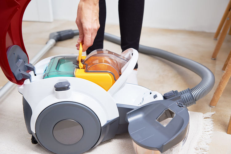 Woman takes out container of dust from vacuum cleaner. household appliances service