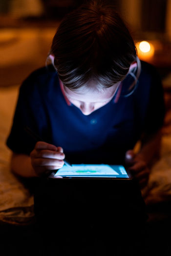 Teenager drawing on tablet with bright screen and stylus in low light