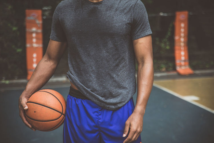 Midsection of man holding basketball ball on court