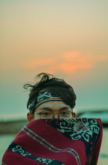 Portrait of man holding scarf against sky during sunset