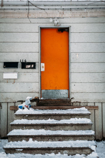 Centered composition of orange door on snow steps.