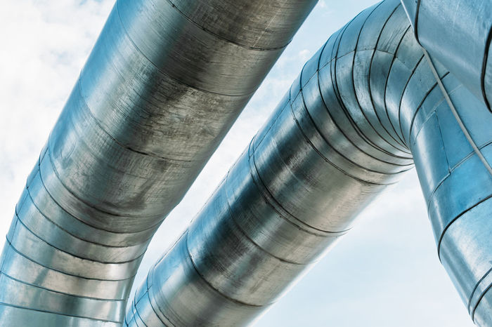 Low angle view of metallic pipes against sky