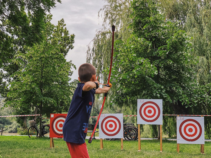 Side view of boy practicing archery against trees