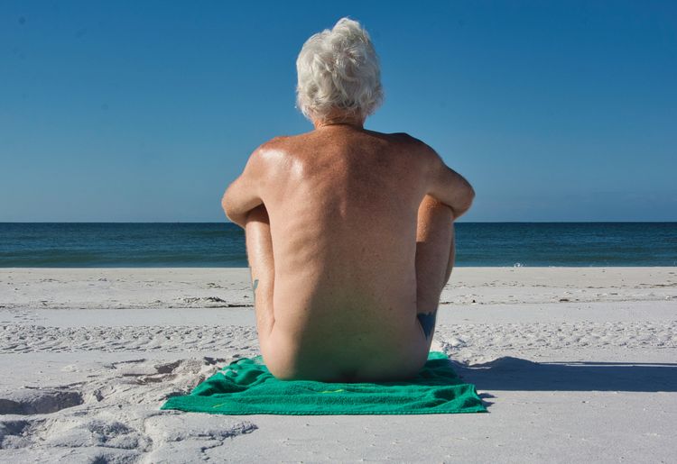 Rear view of shirtless man on beach watching the waves come in
