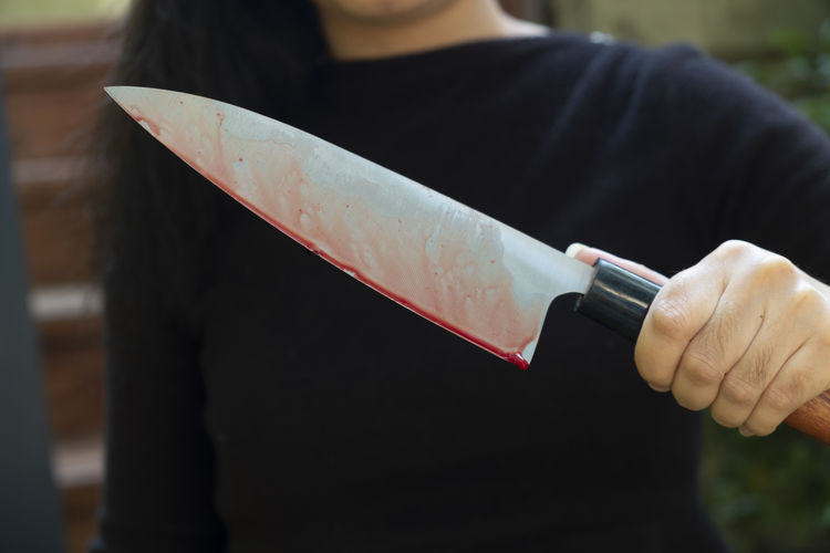 Midsection of woman holding blood covered knife