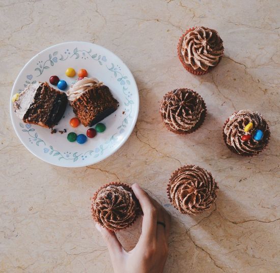 Cropped image of woman holding homemade chocolate cupcake on table