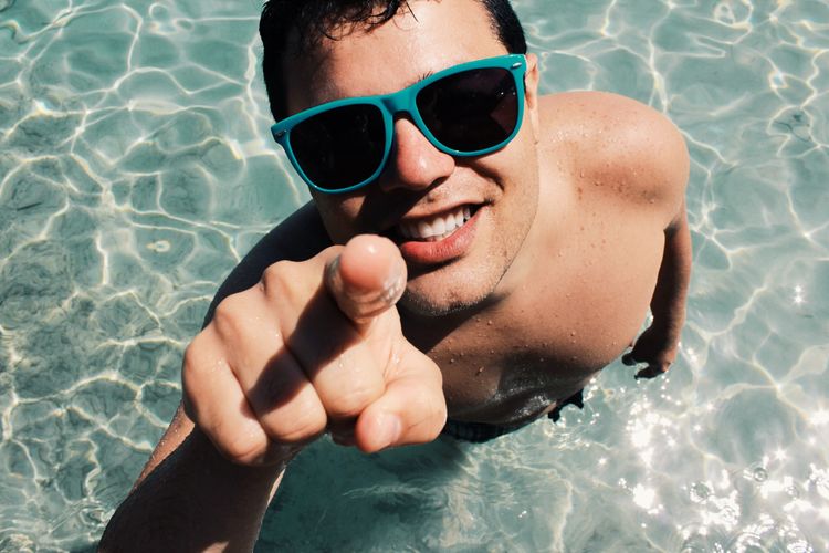 High angle portrait of shirtless mature man wearing sunglasses while standing in swimming pool