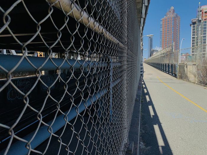 Chainlink fence against sky in city with bike lane over nyc bridge