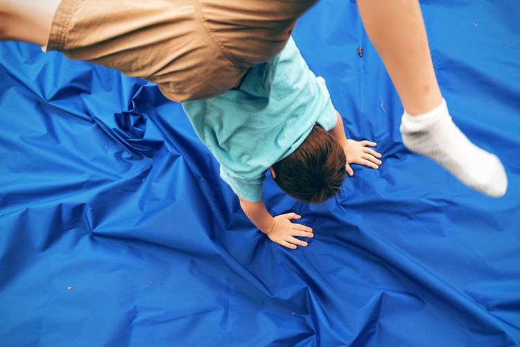 High angle view of boy performing handstand on blue fabric in yard