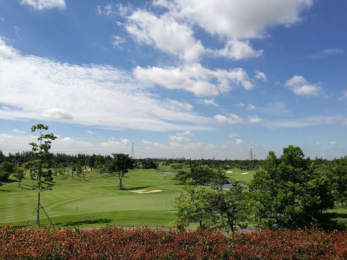 Scenic view of golf course against cloudy sky 
