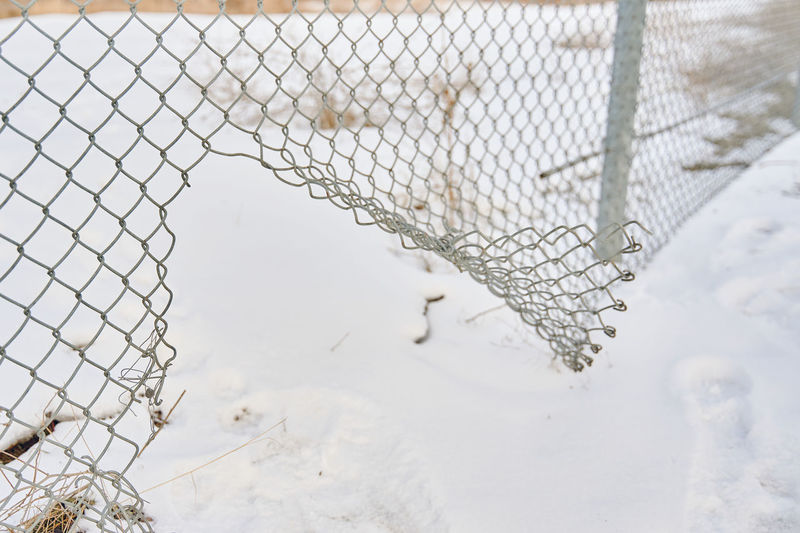High angle view of snow covered field seen through chainlink fence