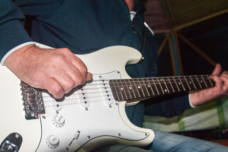 A man plays a white electric guitar