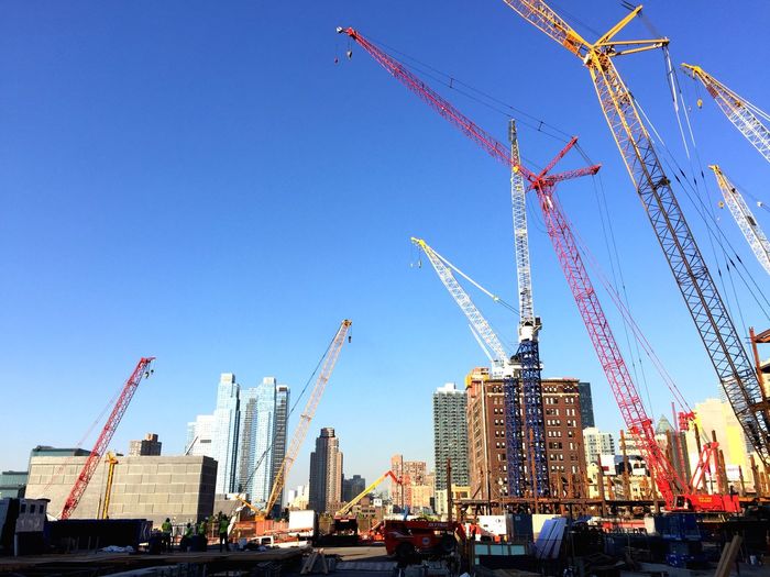 Low angle view of cranes against clear sky at commercial dock